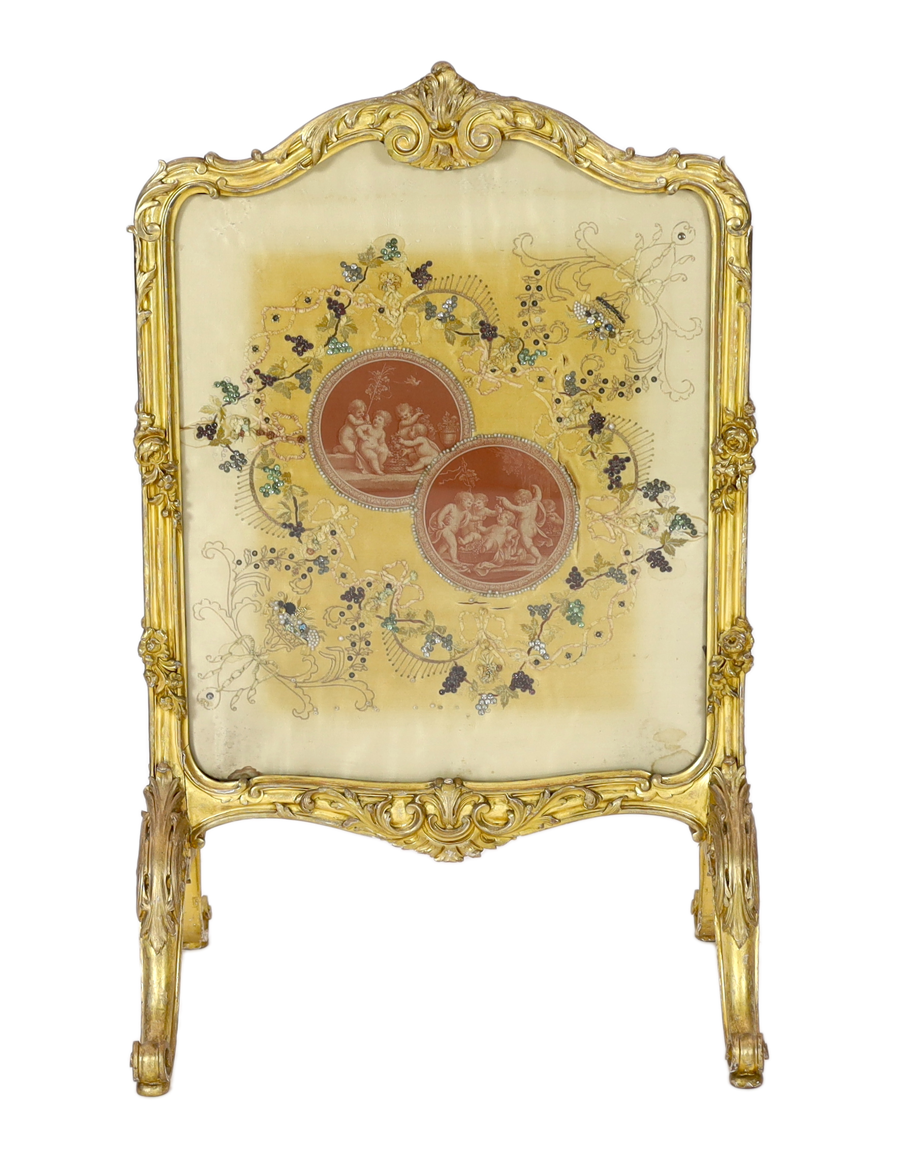 A Louis XV style carved giltwood framed fire screen, the silk panel printed with roundels of playful amorini, within naturalistic beadwork decorated foliage, 60cm wide, 93cm high. Condition - poor to fair, Please note th